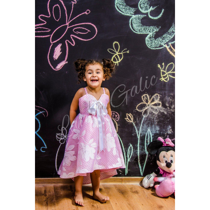Rochie Joselina Mini roz cu buline, flori mari și fundă albă, purtată de o fetiță