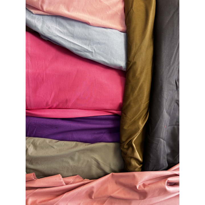 Materiale textile în nuanțe de roz, gri, mov, kaki și negru, așezate în straturi